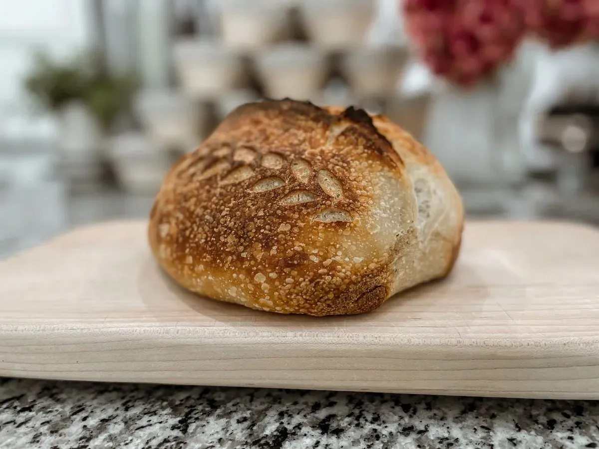 A single round sourdough boule with a hand-scored wheat pattern on a wooden board