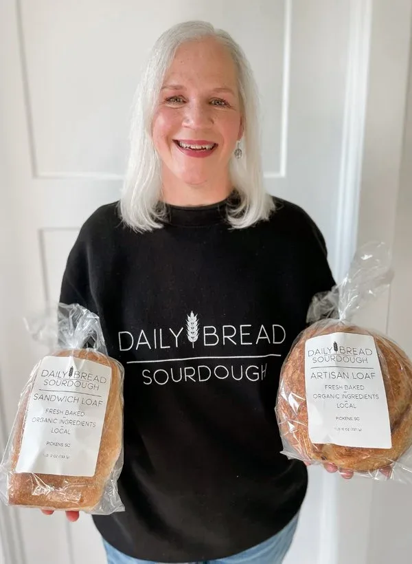 Lynn Addis, founder and baker of Daily Bread Sourdough, holding two fresh loaves